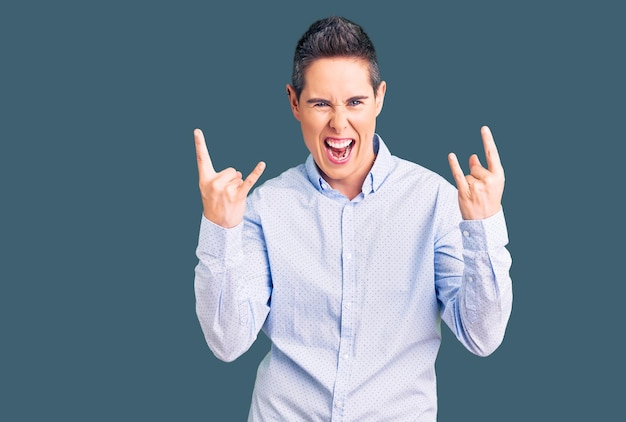 Young woman with short hair wearing business clothes shouting with crazy expression doing rock symbol with hands up music star heavy concept