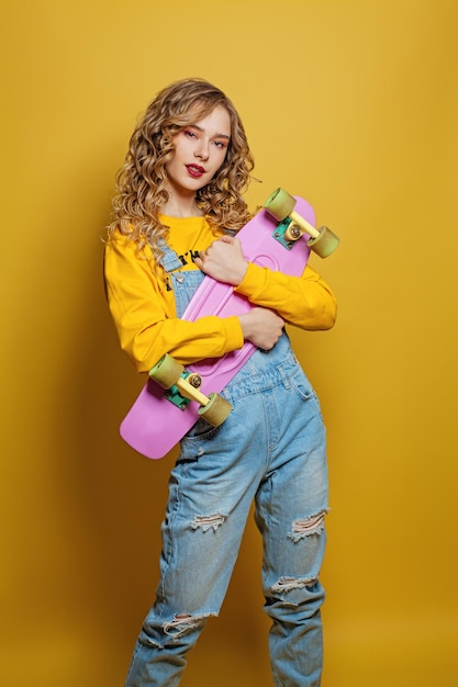 Young woman with skateboard on vibrant yellow background