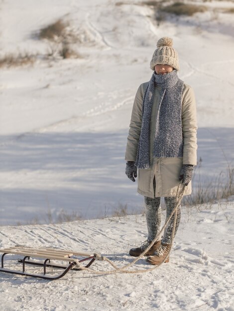 Young woman with sled dressed in casual beautiful trendy winter clothes enjoying winter sports games