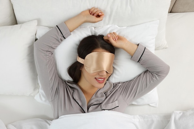 Young woman with sleeping mask in bed top view