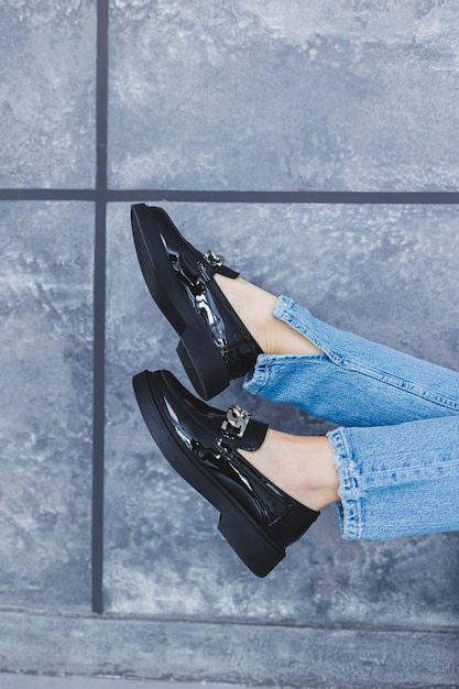 Молодая женщина с стройными красивыми ногами в модных черных кожаных туфлях сидит на стуле в студии Женские стильные мокасины крупным планом Весенняя коллекция обуви