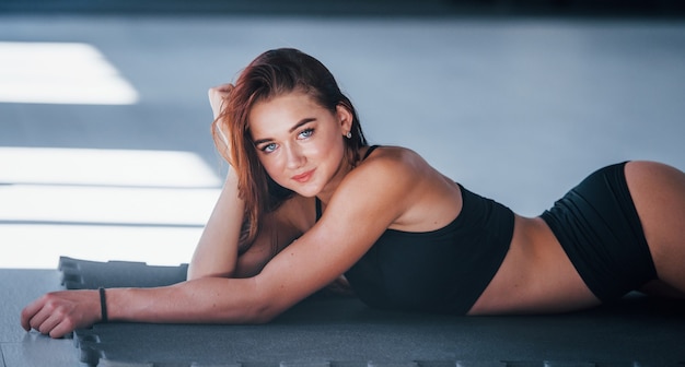 Young woman with slim type of body and in black sportive clothes lying down on the fitness mat.