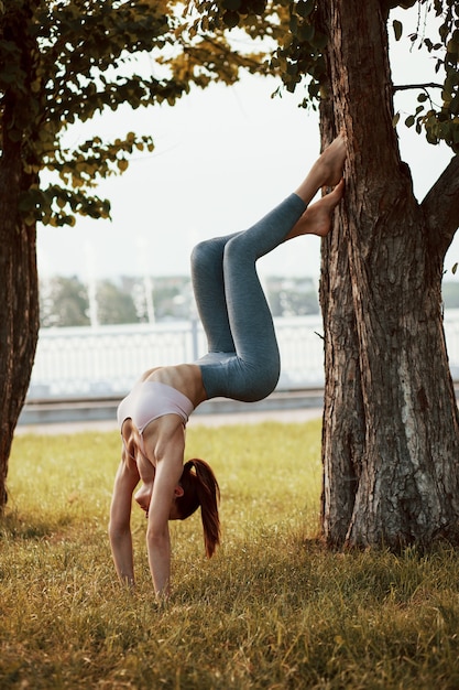 Young woman with slim type of body does exercises in the park