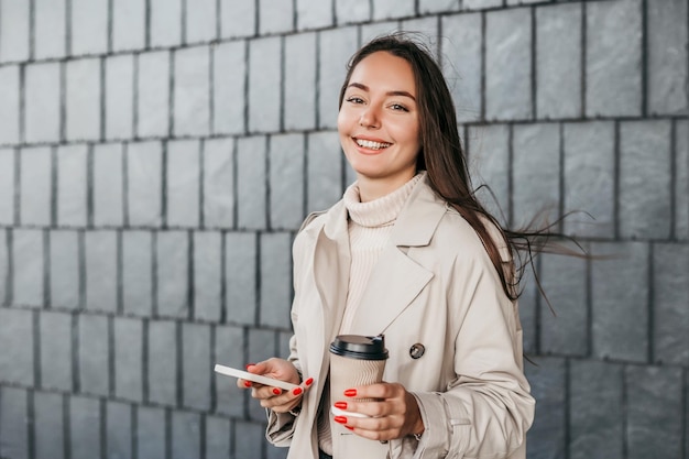 A young woman with a smartphone stands against the background of the facade of the building