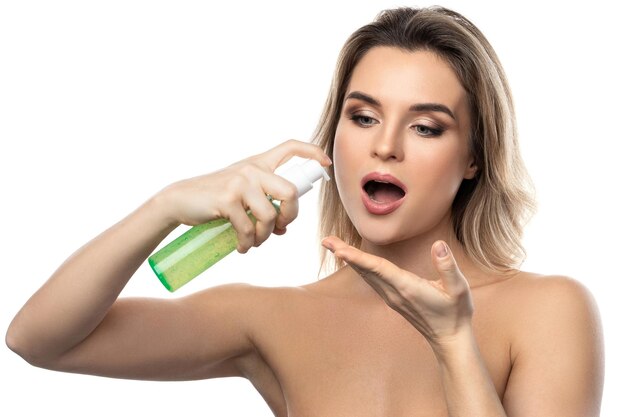 Young woman with a smooth skin holding a bottle of green cleansing gel on white background