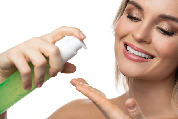Young woman with a smooth skin holding a bottle of green cleansing gel on white background