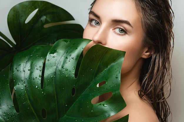 Monstera deliciosa 식물 잎을 들고 매끄러운 피부를 가진 젊은 여자