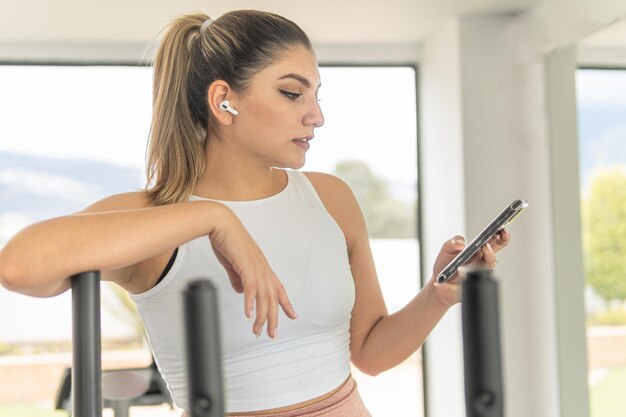Молодая женщина с спортивным топом выбирает музыку на своем сотовом телефоне, чтобы слушать с помощью беспроводных наушников