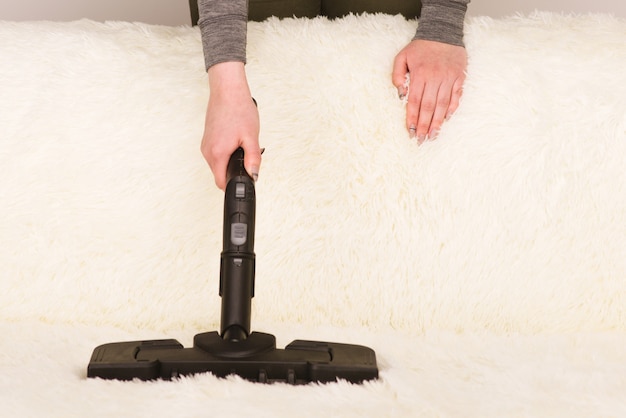 Giovane donna con un pulitore a vapore pulisce il tappeto sul divano