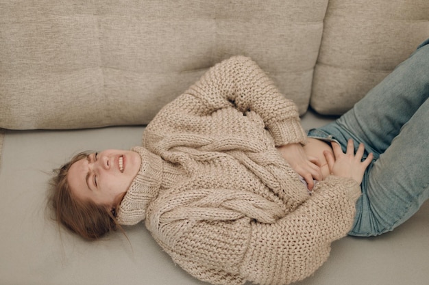 Young woman with stomach abdominal pain ache lying on sofa