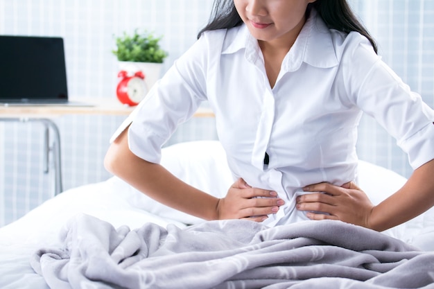 Young woman with stomach ache sitting on bed