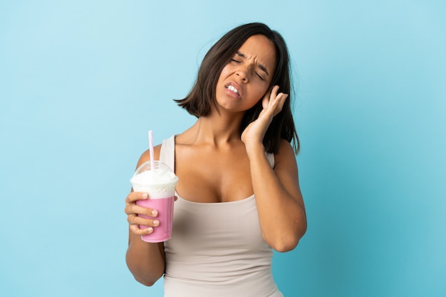 Young woman with strawberry milkshake on blue with headache