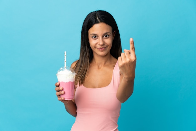 Young woman with strawberry milkshake doing coming gesture