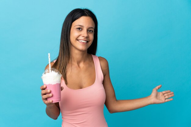 Young woman with strawberry milkshake extending hands to the side for inviting to come