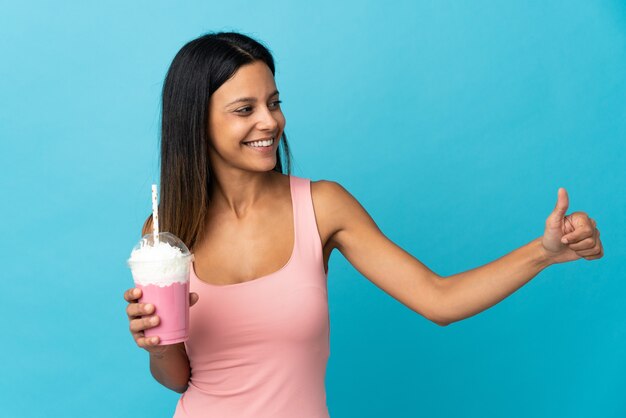 Young woman with strawberry milkshake giving a thumbs up gesture