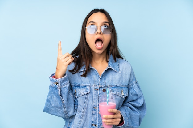 Young woman with strawberry milkshake over isolated blue background pointing up and surprised