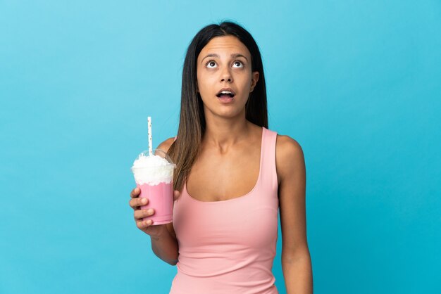 Young woman with strawberry milkshake looking up and with surprised expression