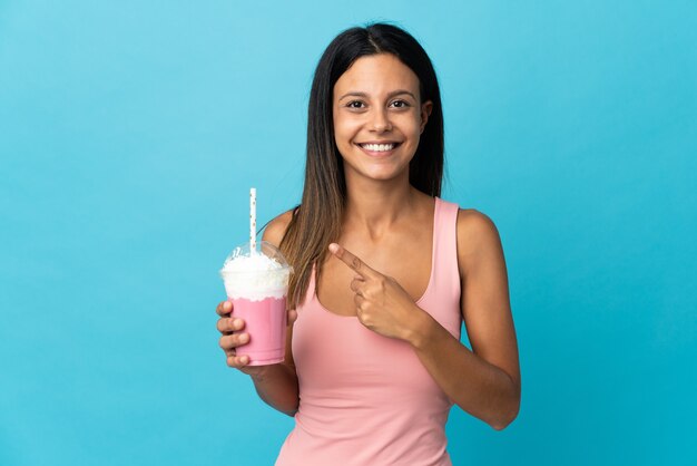 Young woman with strawberry milkshake pointing to the side to present a product