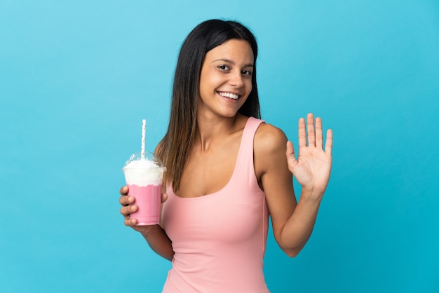 Young woman with strawberry milkshake saluting with hand with happy expression