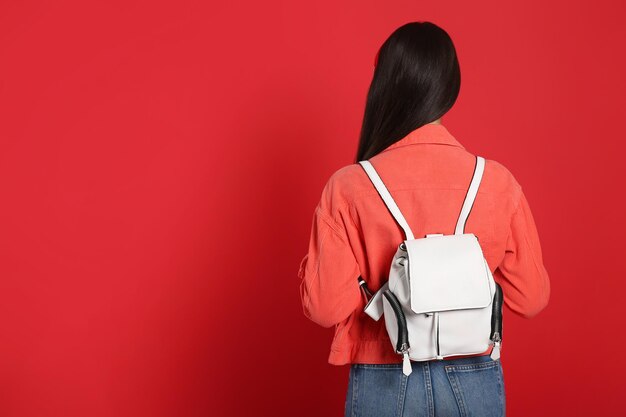 Young woman with stylish leather backpack on red background back view Space for text