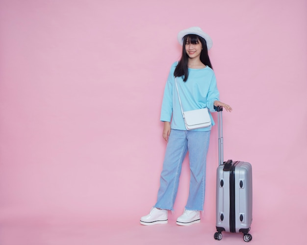 Young woman with suitcase on pink wall