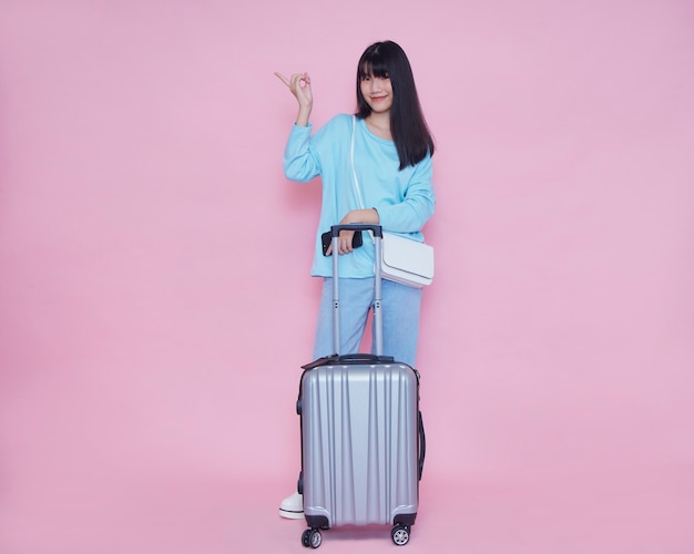 Young woman with suitcase on pink wall