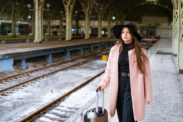 週末を楽しむ電車を待っている駅の旅行者の女の子のプラットフォームにスーツケースを持つ若い女性...