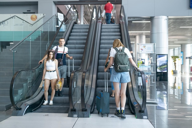 スーツケースを持った若い女性と、空港で飛行機に搭乗し、フライトをチェックしているバックパックを持った観光客。旅行のコンセプト