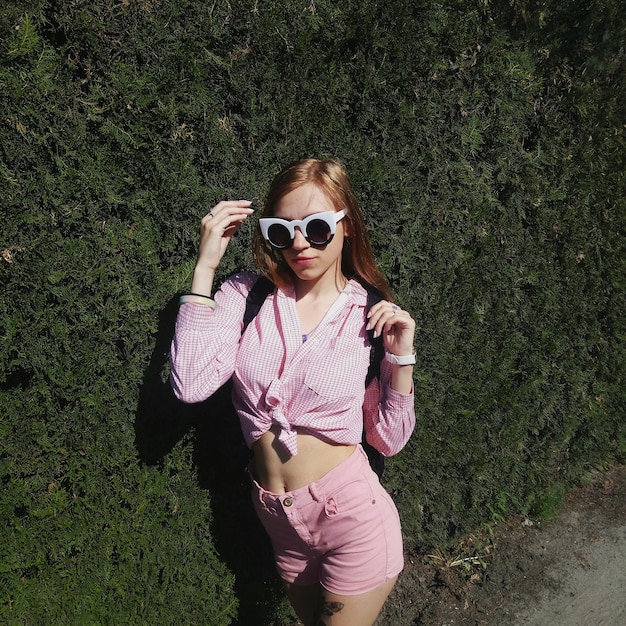 Young woman with sunglasses standing by hedge