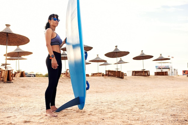 Photo young woman with a surf stands on the beach waiting for a ride