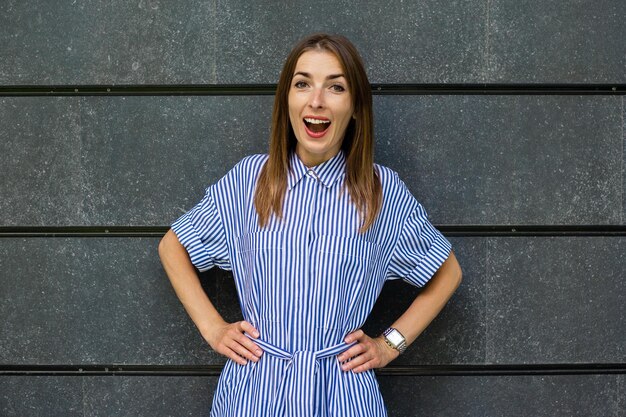 Young woman with a surprised face in a dress on the background of a stone wall