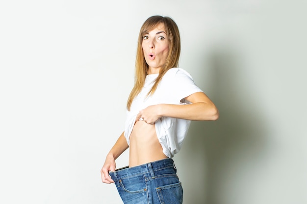 Young woman with a surprised face in oversize jeans on a light background