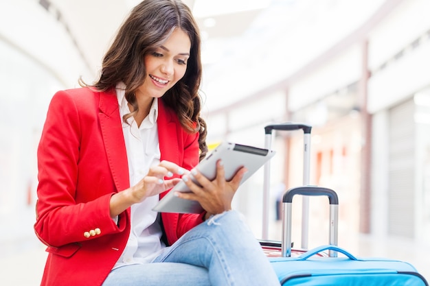 흐릿한 공항 배경에 태블릿과 여행가방을 들고 있는 젊은 여성