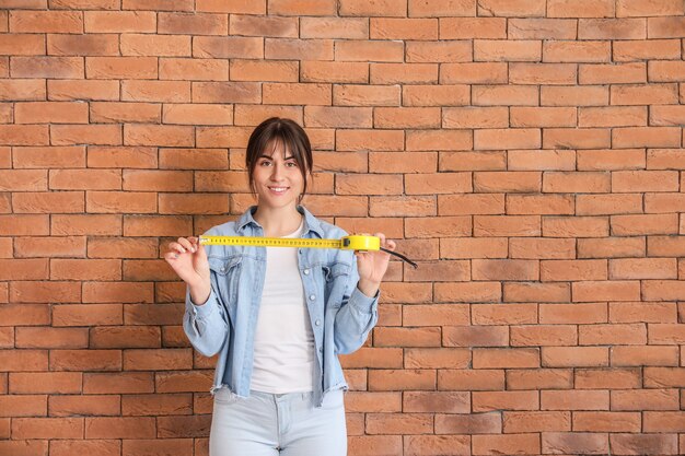 Young woman with tape measure near brick wall