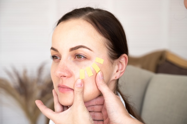 Young woman with tapes on face. Beautician applying yellow kinesio tapes face. Lifting skin and aesthetic taping concept. High quality photo