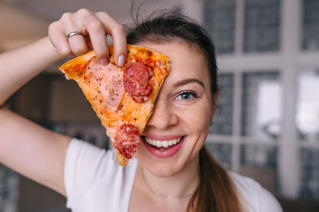 Young woman with tasty pizza laughing in kitchen