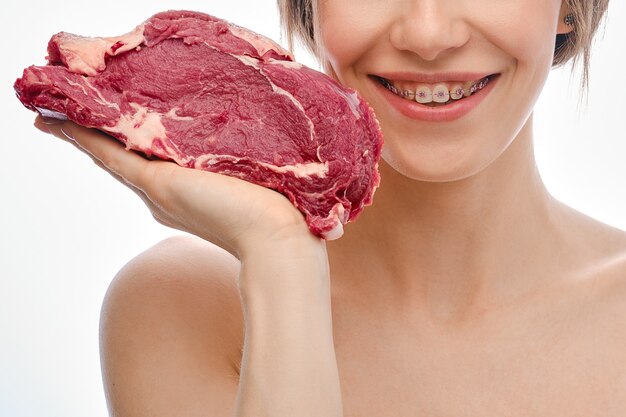 Young woman with teeth with braces holds raw beef meat on palm of her hand