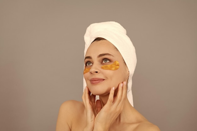 Young woman with terry towel use facial golden eye patch for skin skin