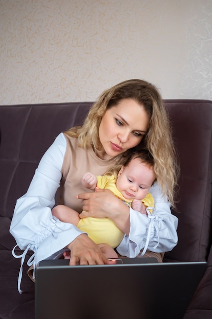 Young woman with toddler in arms typing on laptop, concept of female freelancers on maternity leave