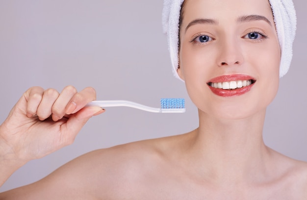 A young woman with a toothbrush smiles broadly. Close-up.