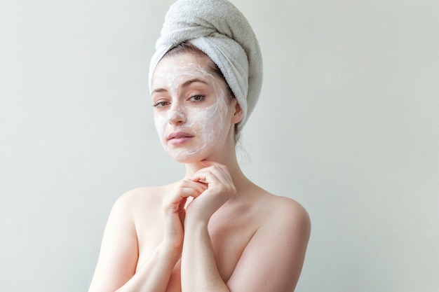 Giovane donna con un asciugamano sulla testa che applica maschera nutriente bianca