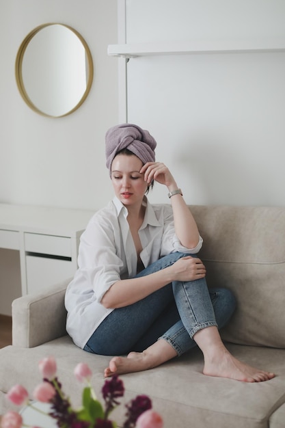 young woman with a towel on head looking in the mirror and apply cream on face skin