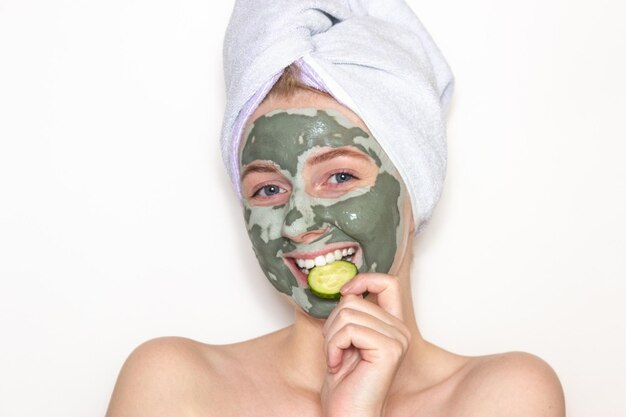 Photo a young woman with a towel on her head and a clay mask on her face and a piece of cucumber