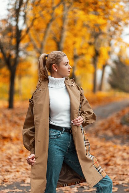 young woman with a trendy hairstyle in an elegant coat poses outdoors in a park