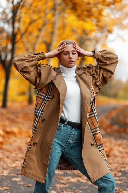 young woman with a trendy hairstyle in an elegant coat poses outdoors in a park