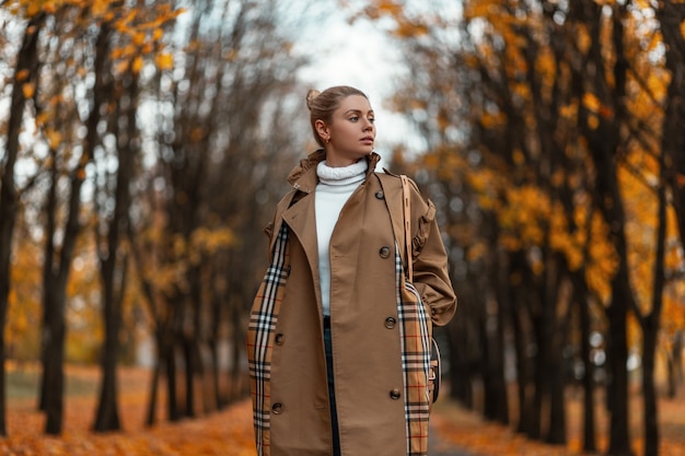 young woman with a trendy hairstyle in an elegant coat poses outdoors in a park