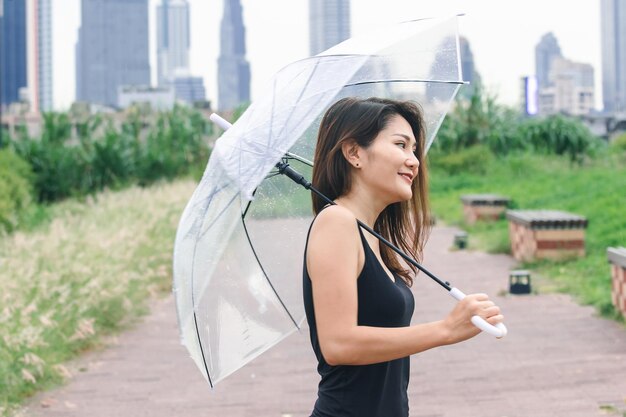 写真 雨の中に立っている傘をかぶった若い女性