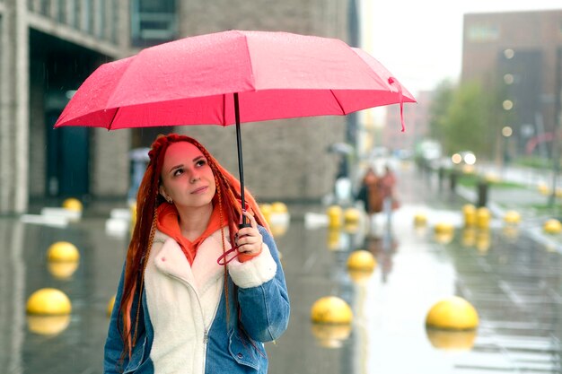 Young woman with umbrella on street Positive young female in warm clothes smiling while standing on city street