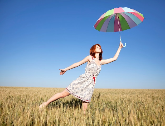 Young woman with umbrella on wheat field in summer time.