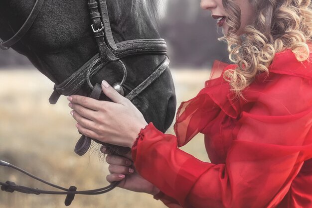 Foto giovane donna con abito vintage, coccole delicatamente un cavallo, accarezzandogli la testa.